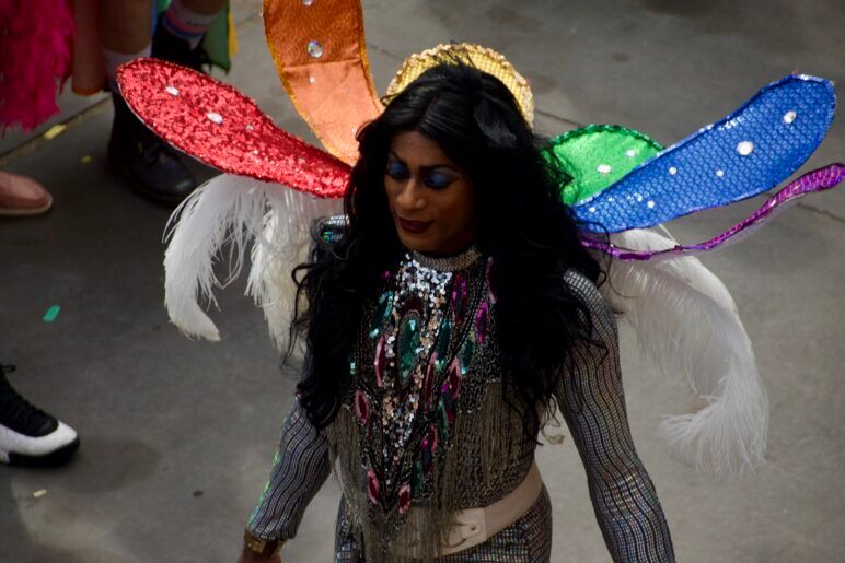 A gorgeous queen struts confidentially while wearing rainbow colored dragonfly wings