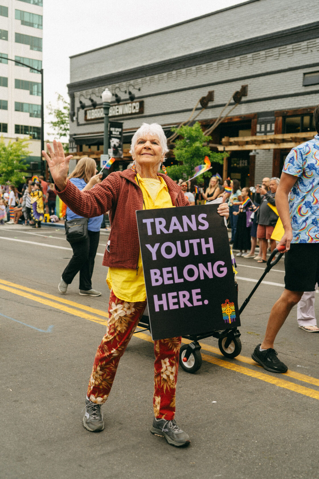 A woman marches in Boise Pride parade with a sign that reads "Trans youth belong here."