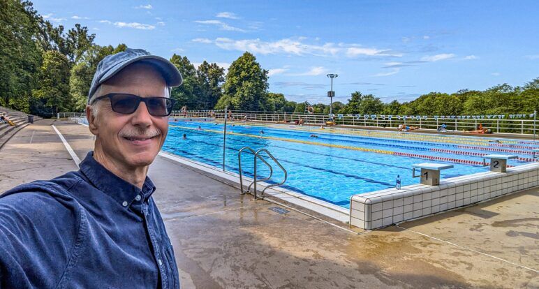 Michael standing in front of an outdoor swimming pool on a sunny Sunday. Michael Jensen stands next to the pool where he had an accident.