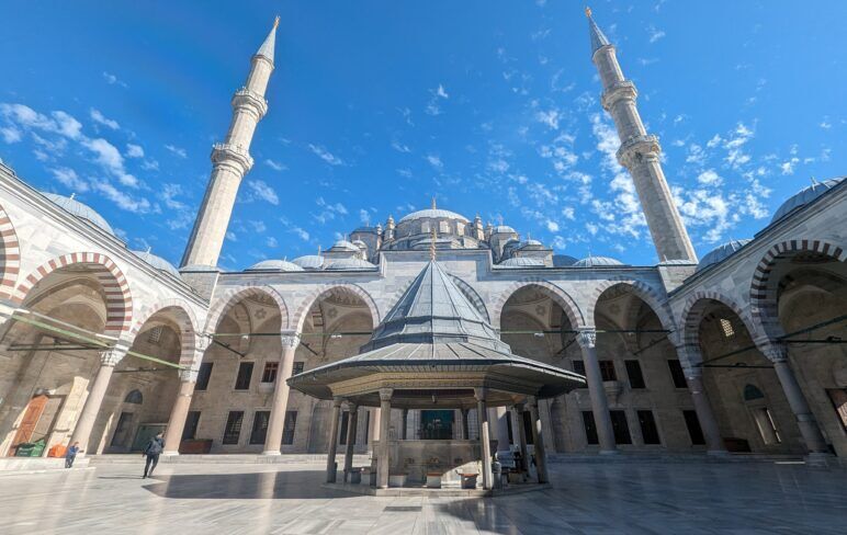 The white courtyard and minarets of the Fatih Mosque under a bright blue sky. View of the Fatih mosque courtyard