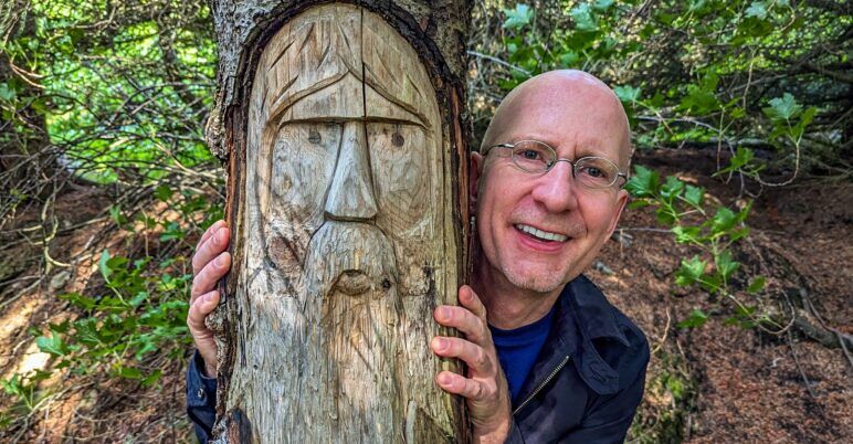 The author poses next to a face carven into a tree