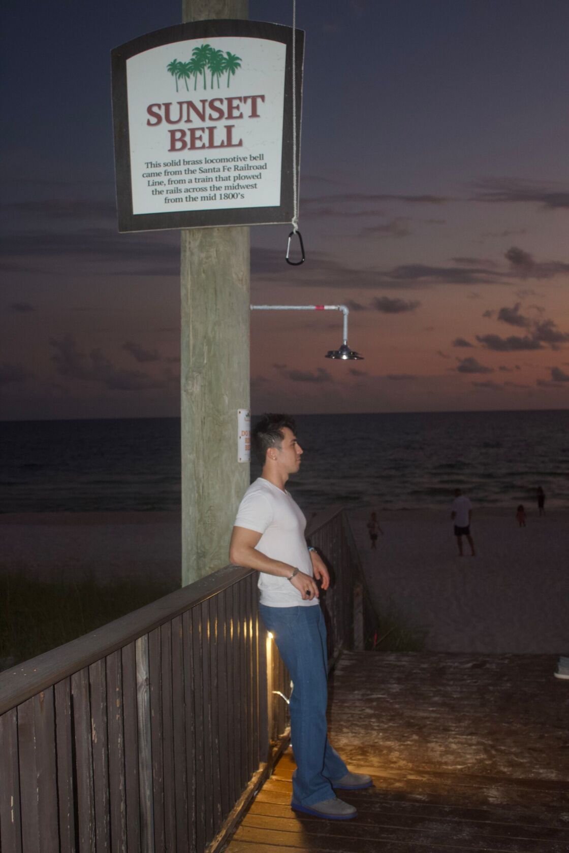 Author wearing white shirt and blue jeans, standing in front of the beach at Runaway Island restaurant. 
