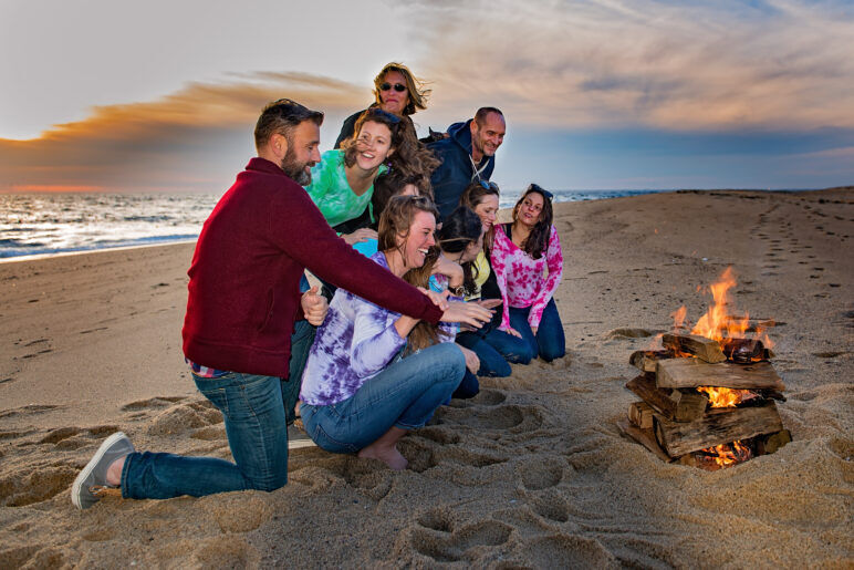 A group of people sit around a campfire on the beach