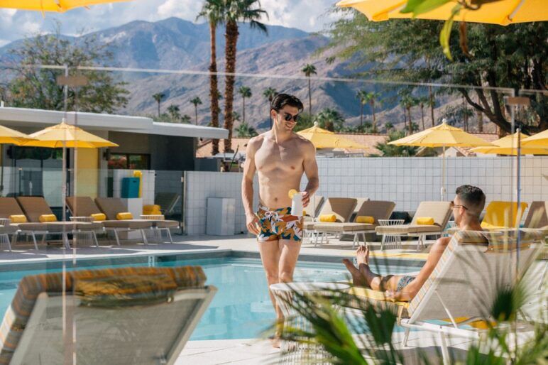 A shirtless man walks past a man in a pool chair at a Palm Springs resort