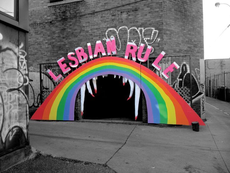 Entrance to Killjoy's Kastle- A rainbow with teeth with the words "lesbian rule" above it