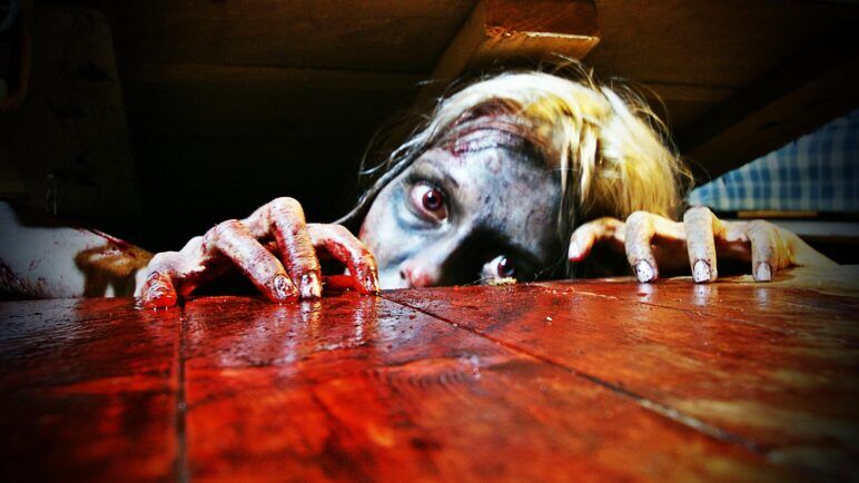 A scary image of a women crawling out of the floor covered in blood
