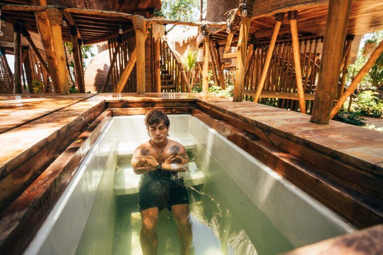 A young man with tattoos takes a cold plunge in a tree house.