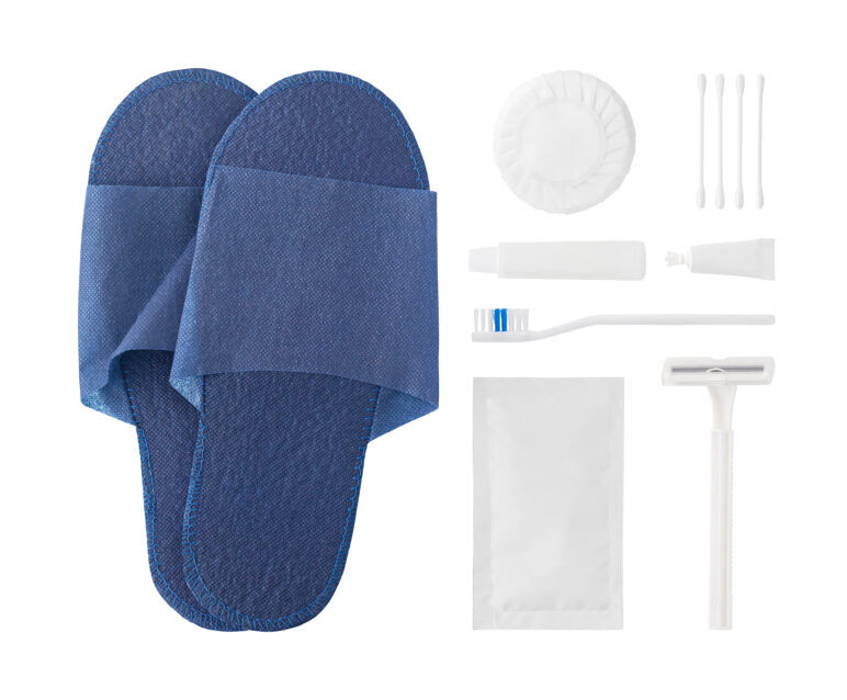A set of complimentary hotel toiletries, including disposable slippers, a toothbrush, toothpaste, a razor, soap, and cotton swabs, neatly arranged on a white background.