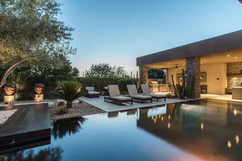 A pool shimmers in front as it leads into a mansion