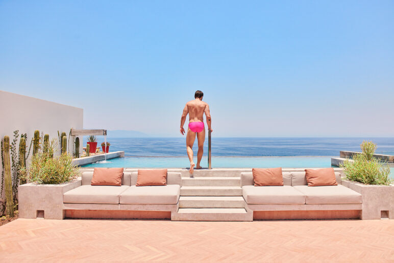 A man stands at the edge of a pool wearing a pink speedo