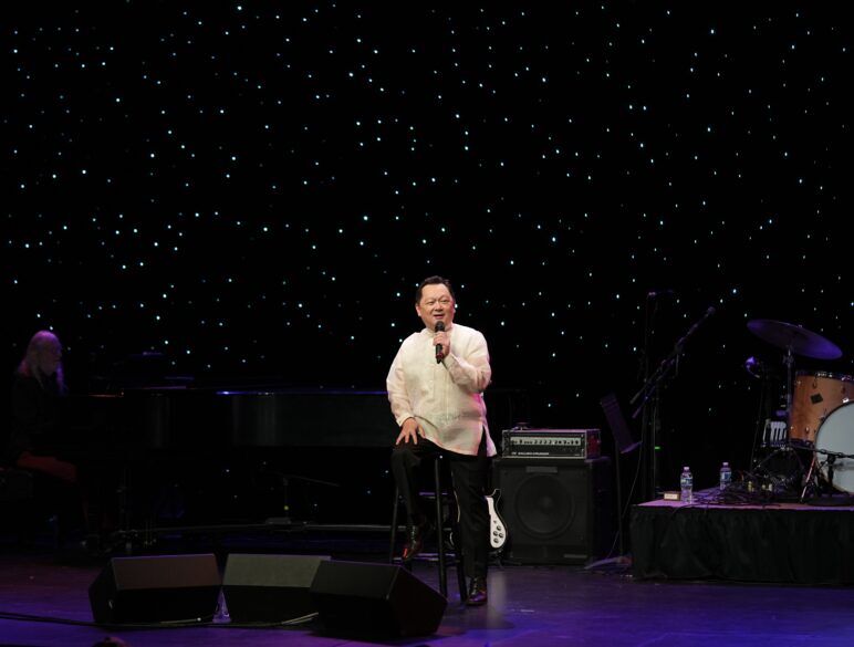 A Filipino man stands on stage holding a microphone