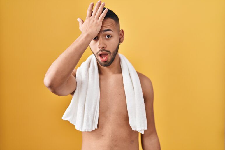 Shirtless man with a towel over his shoulders, holding his forehead in a playful "oops" expression against a yellow background.