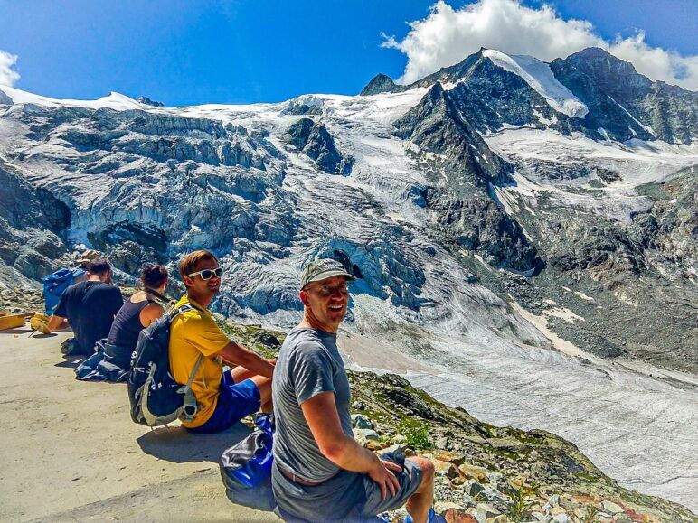 Five people sit on a ledge overlooking Moiry Glacier.