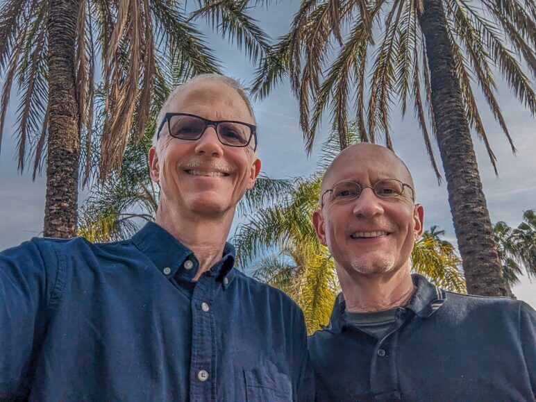 The author and his husband pose for a selfie in front of palm trees.