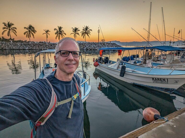 The author poses for a selfie in front of a marina at sunrise