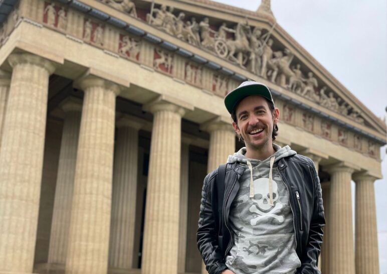 Ian smiles while wearing a leather jacket and hoodie in front of the Parthenon replica in Nashville.