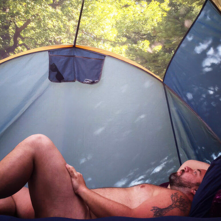 A man without clothes lays next to a tent