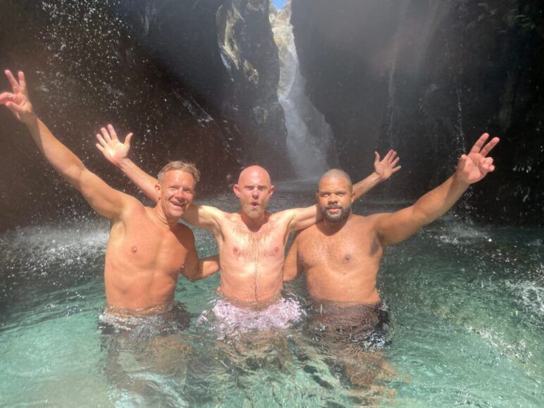 Three older men stand in a natural pool