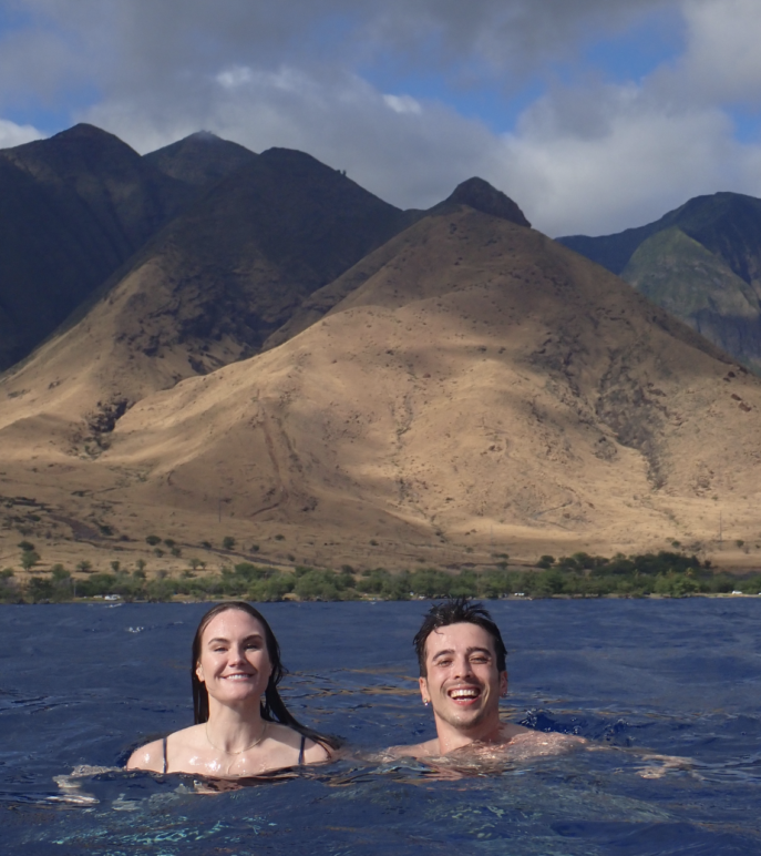 Author and friend Nora swimming in the sea with mountains behind them. 