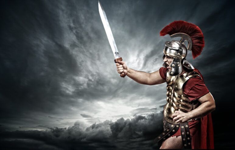 A Roman soldier wearing armor waving a sword with a dark sky behind him. 