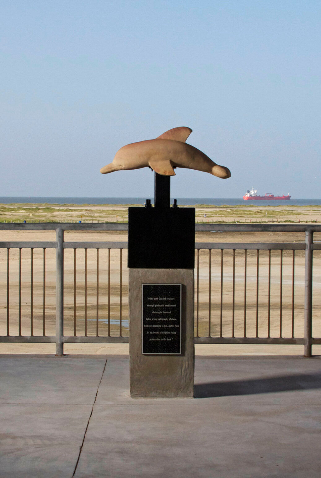 The Pink Dolphin Statue in Galveston, Texas with a pink ship in the background at sea. 