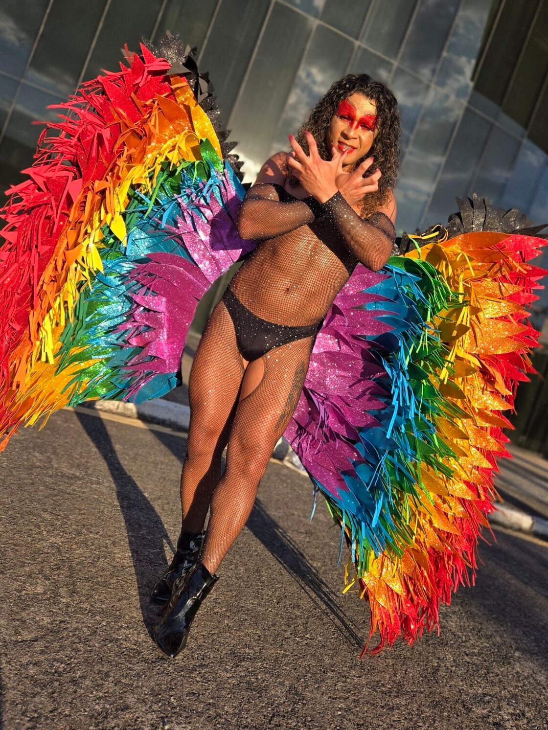 A drag performer with rainbow colored butterfly wings poses outdoors at São Paulo Pride.