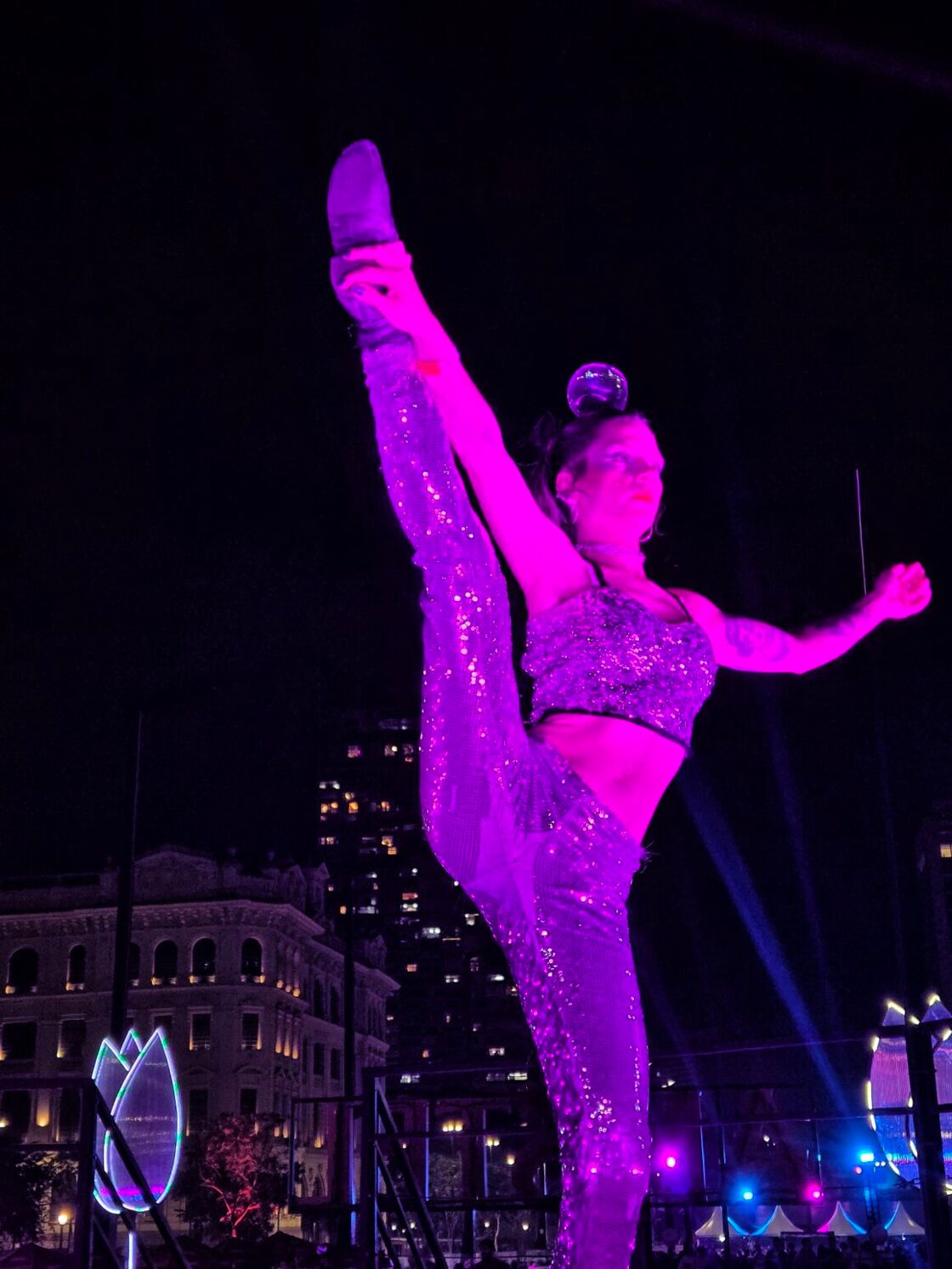 A performer at São Paulo Pride does the butterfly pose while performing in a purple glowing light.