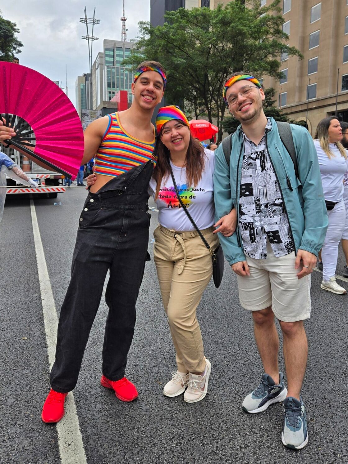 Two men pose smiling on either side of a woman on the streets of the São Paulo parade.
