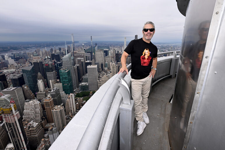 Andy Cohen poses in sunglasses on the balcony of the Empire State Building.