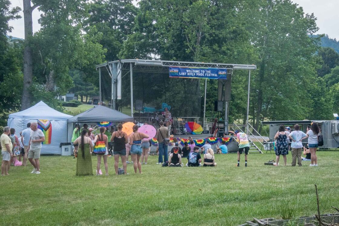 View of a small wooden stage with a few people sitting in the grass around it