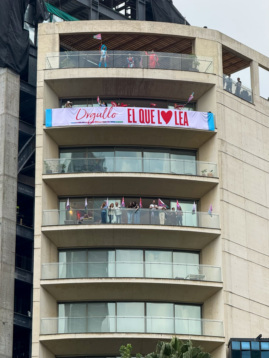 An apartment building in Mexico City where a group of people watch Pride festivities from their balconies.