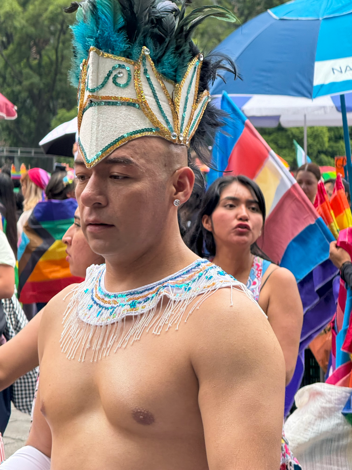 A man wears a sparkling headdress and walks shirtless through Mexico City Pride.