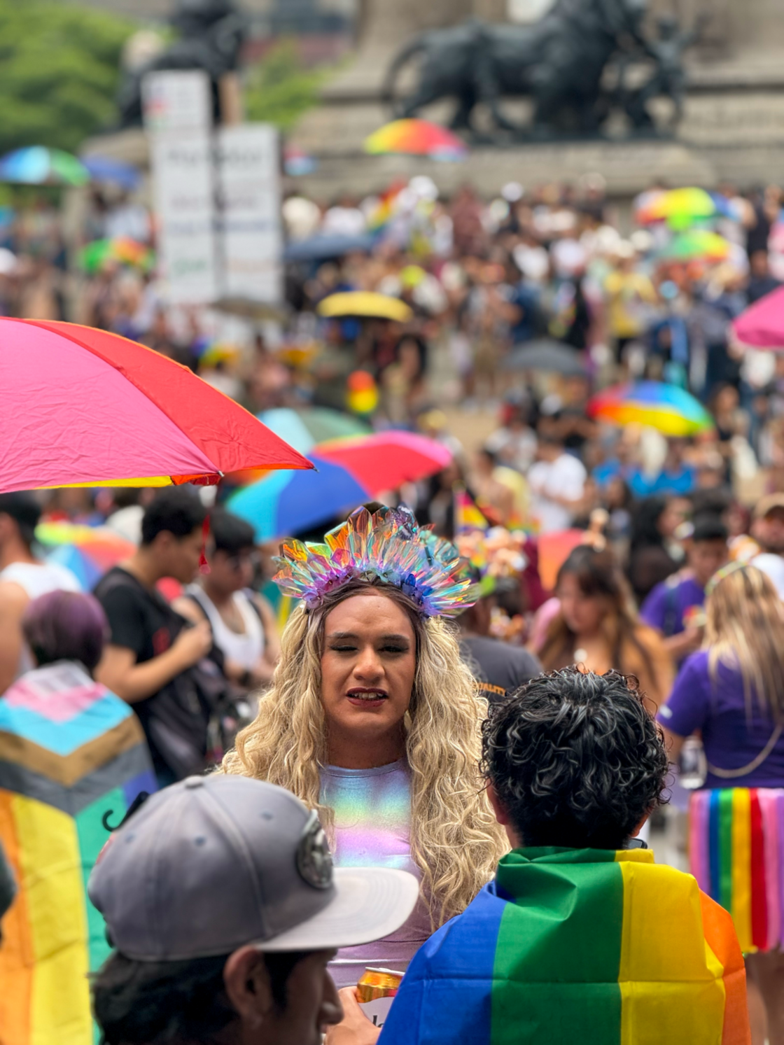 A woman with a rainbow headdress smiles while walking through the crowd at Mexico City Pride.