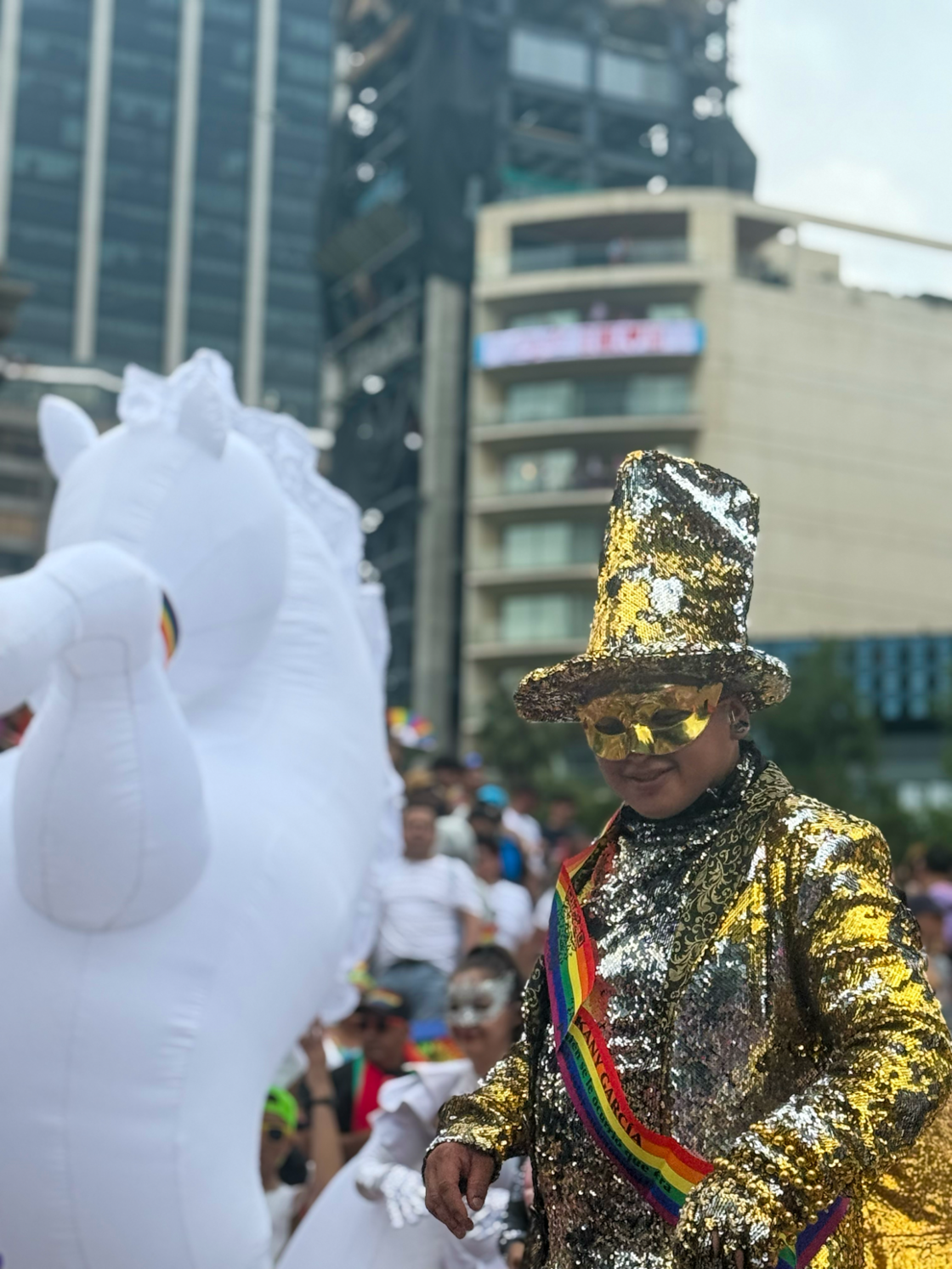 A man in a gold glitter hat and suit wears a masquerade mask at Mexico City Pride.