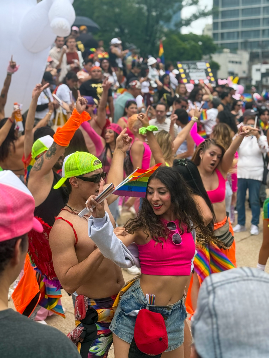 A group of people dance in vibrant colored clothes waving pride flags at Mexico City Pride.