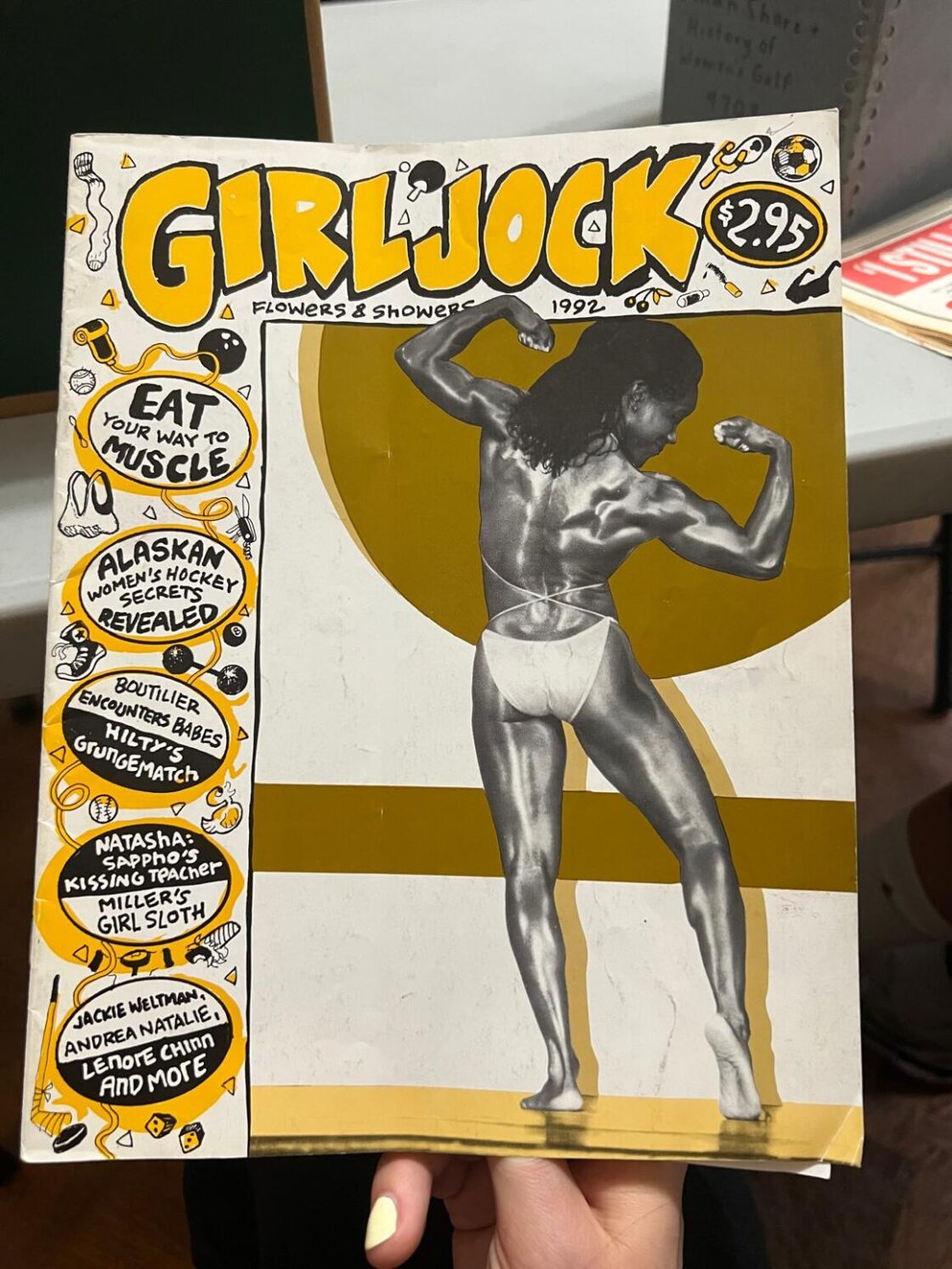 The cover of zine "Girljock" from 1992. Its theme was "Flowers & Showers" and it features a woman flexing in a bikini.