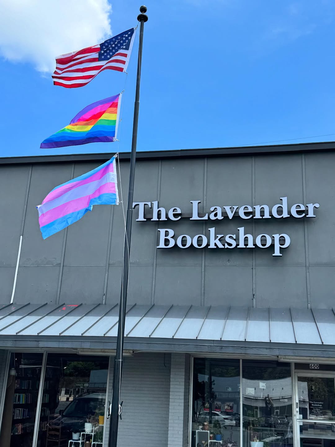 The storefront for The Lavender Bookshop in Marietta, Georgia, which features glass windows and trans and Pride flags hanging from a pole in front.