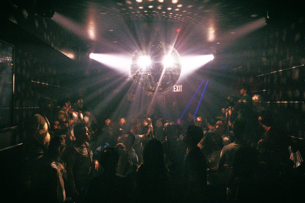 Patrons dance underneath a shimmering disco ball on a packed dance floor at The Ritz Bar & Lounge.