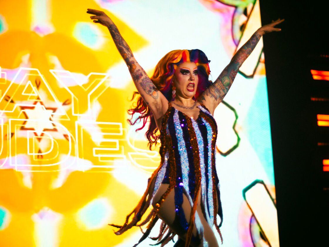 A drag queen in a rainbow wig performs in front of a yellow screen at Bushwig.