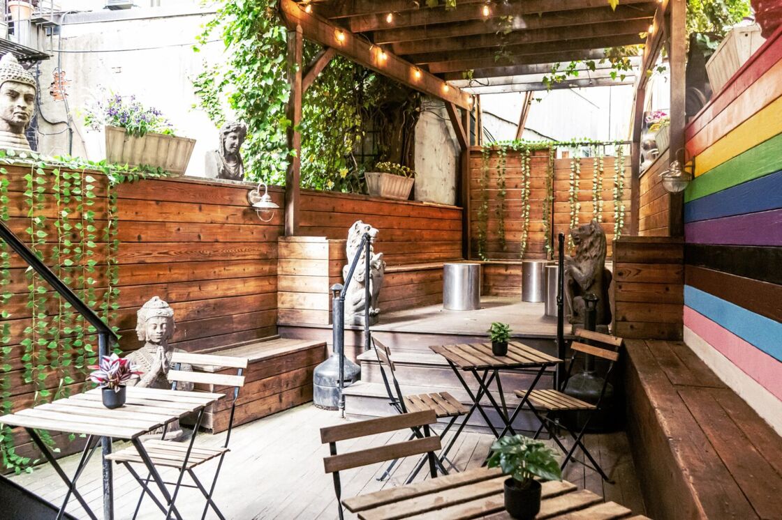 The outdoor patio area at Ritz Bar & Lounge, with a rainbow wooden background in front of benches and wooden tables.