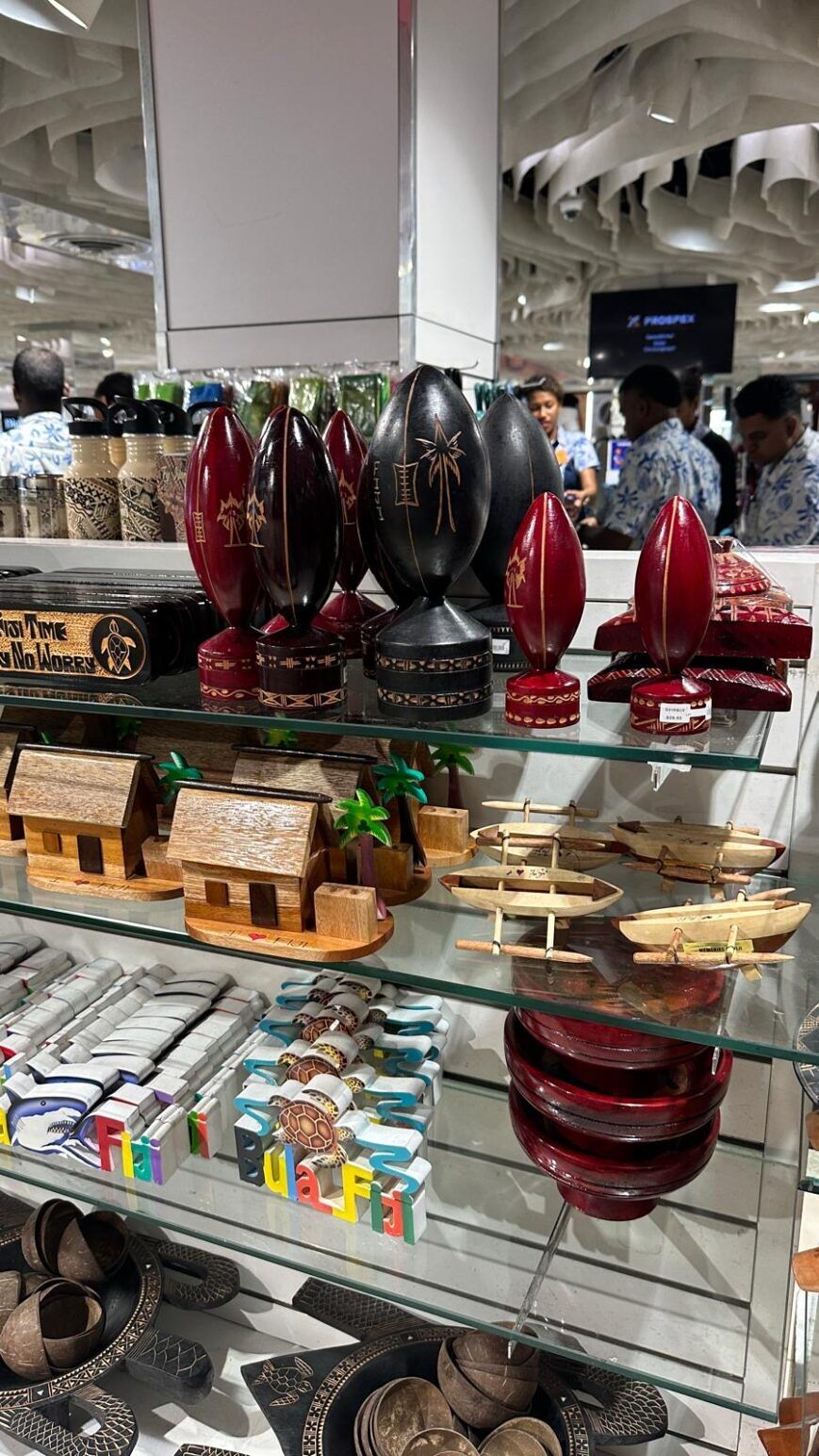A rack of shelves in a Fiji gift shop with various souvenirs, the top shelf featuring rows of rugby statuettes.