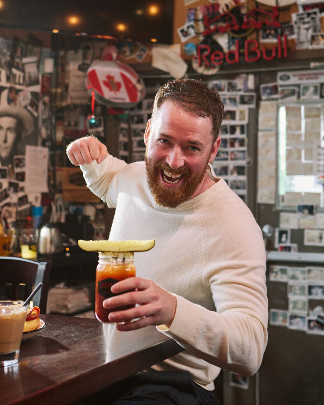 A man with a beard sits in a white sweater at the bar at Leopold's Tavern holding a Bloody Marty in his left hand.