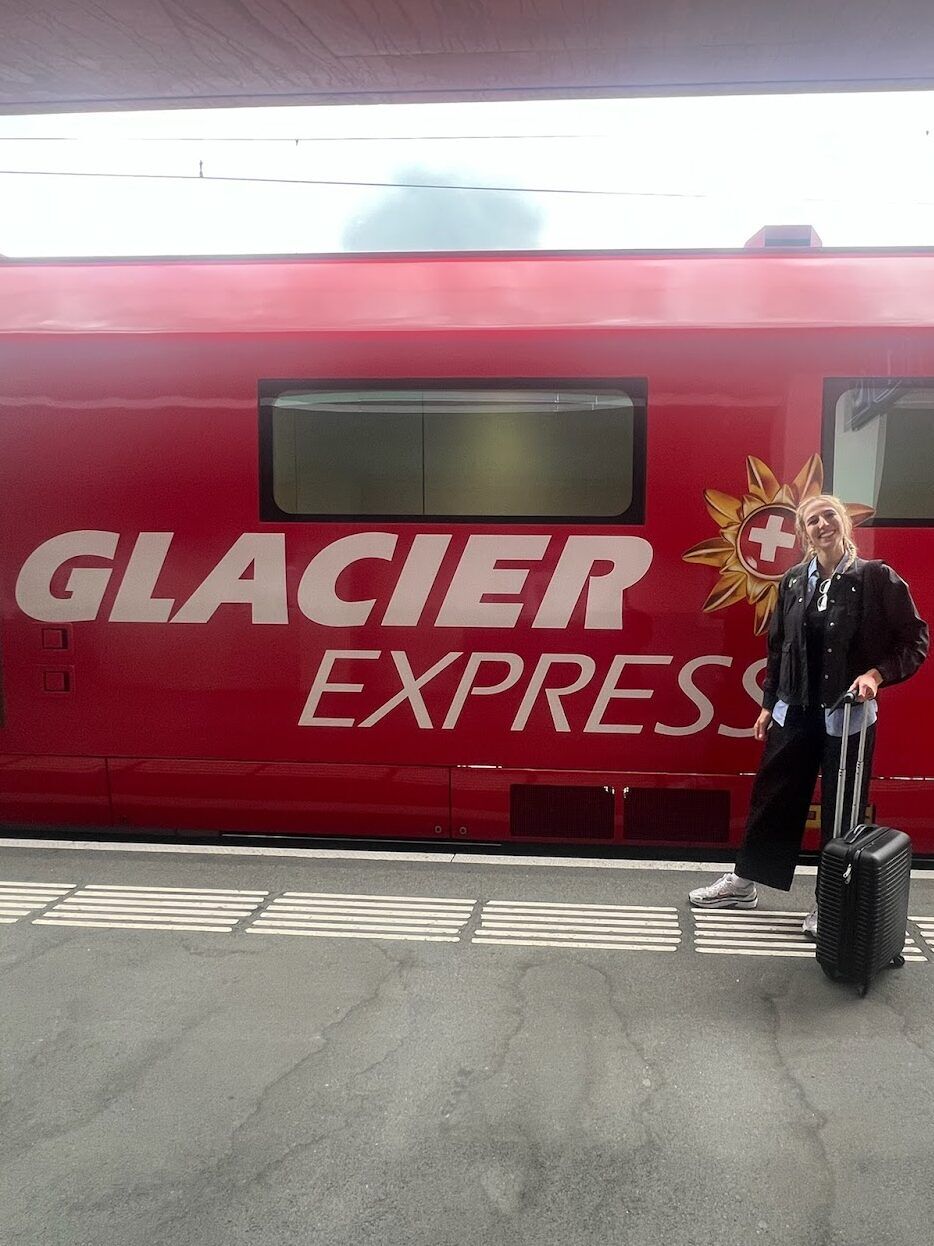 Alexia Garcia stands with her suitcase in front of Switzerland's red Glacier Express train.