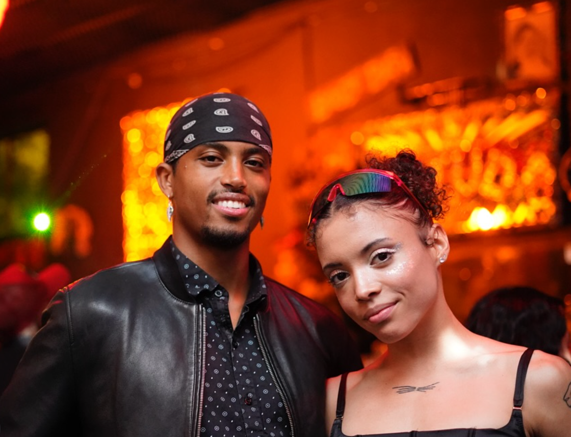 A couple smiles in front of a dimly lit bar at The SEEN Party at The Stud.