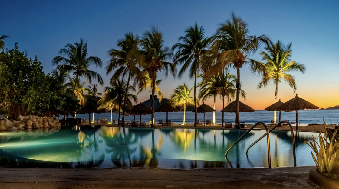 The outdoor and beachside pool at Thompson Zihuatanejo pictured at night, surrounded by palm trees.
