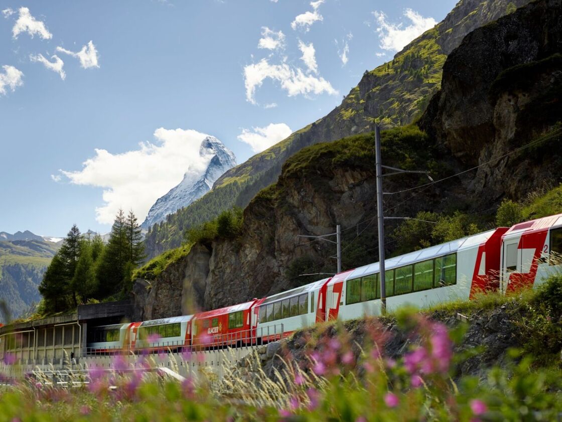 The Glacier Express chugs alongside flowers and a green mountaintop near Zermatt.