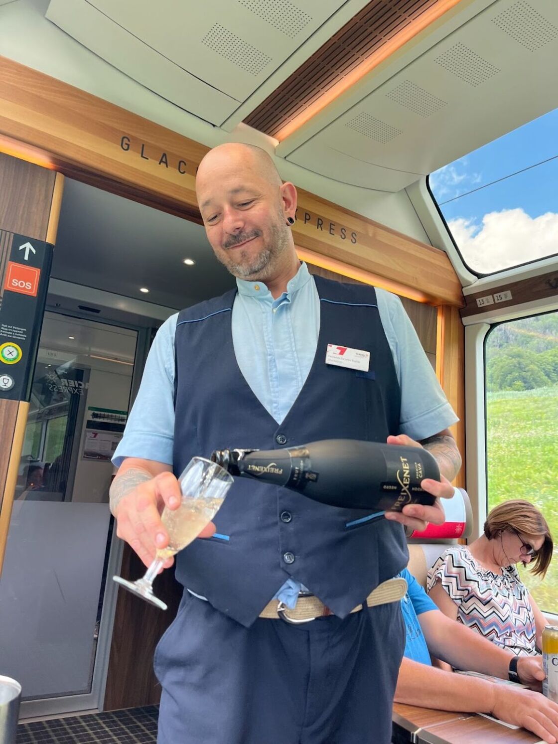 An attendant pours champagne from a bottle into glasses on Switzerland's Glacier Express.