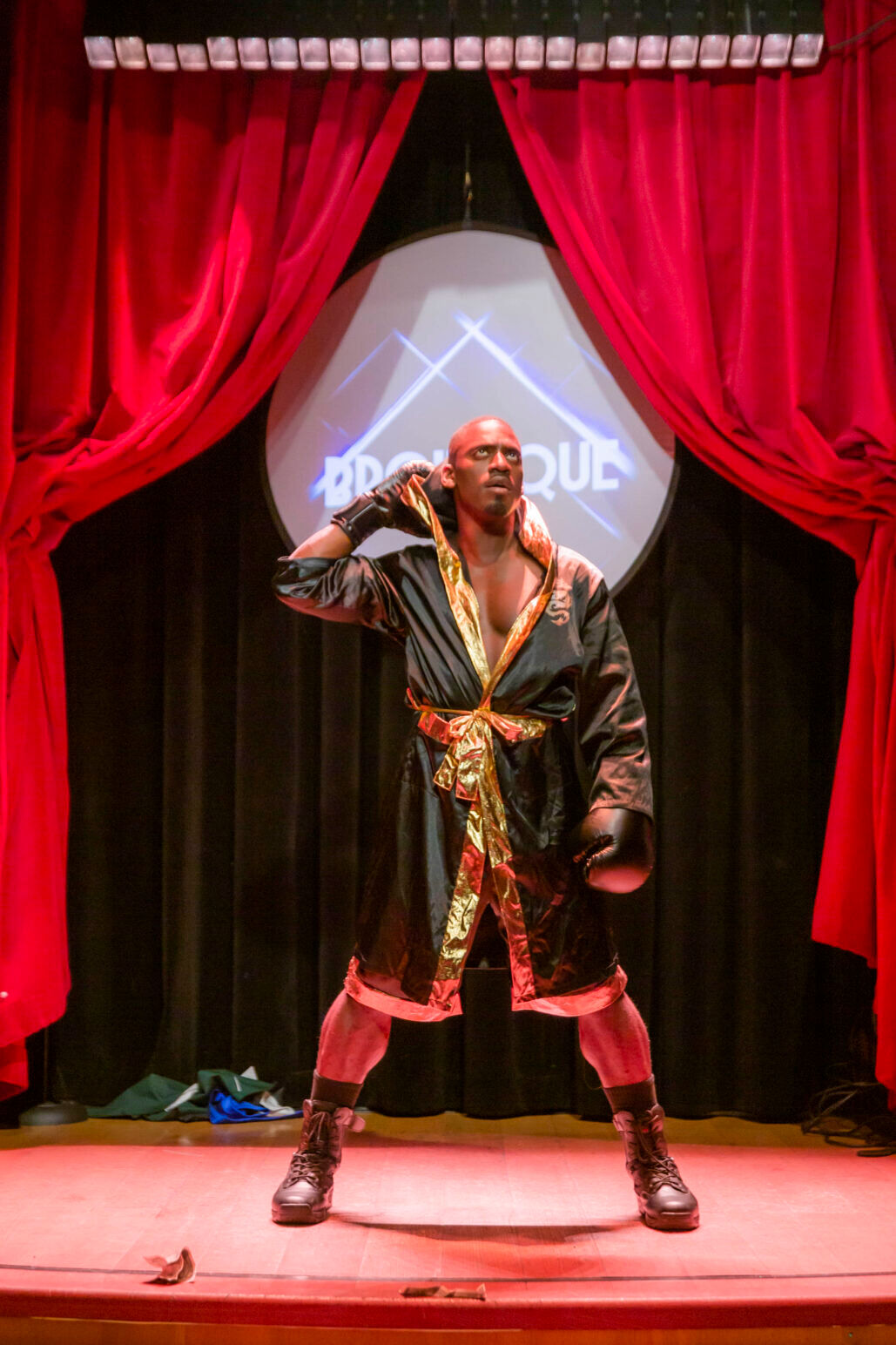 A man poses in a black and golden wrestling robe under spotlights.