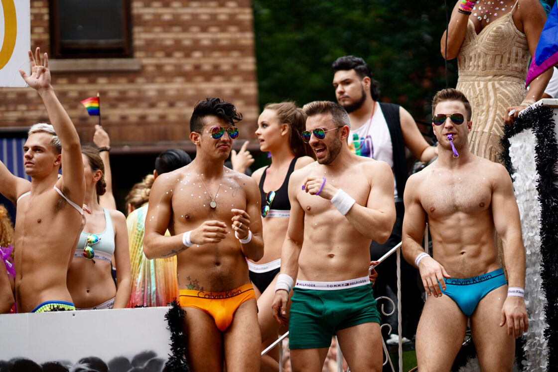 Four shirtless men stand in their underwear outdoors at a Pride festival.