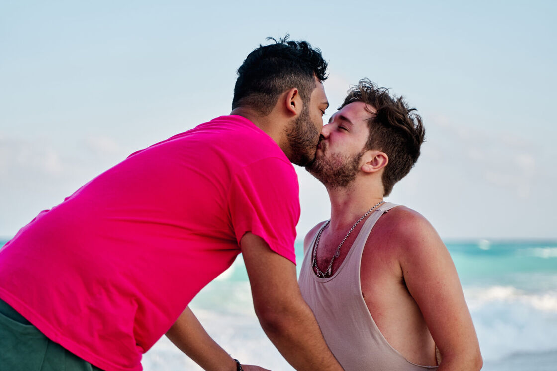 Two gay men kiss in front of the ocean on a Mexican beach.